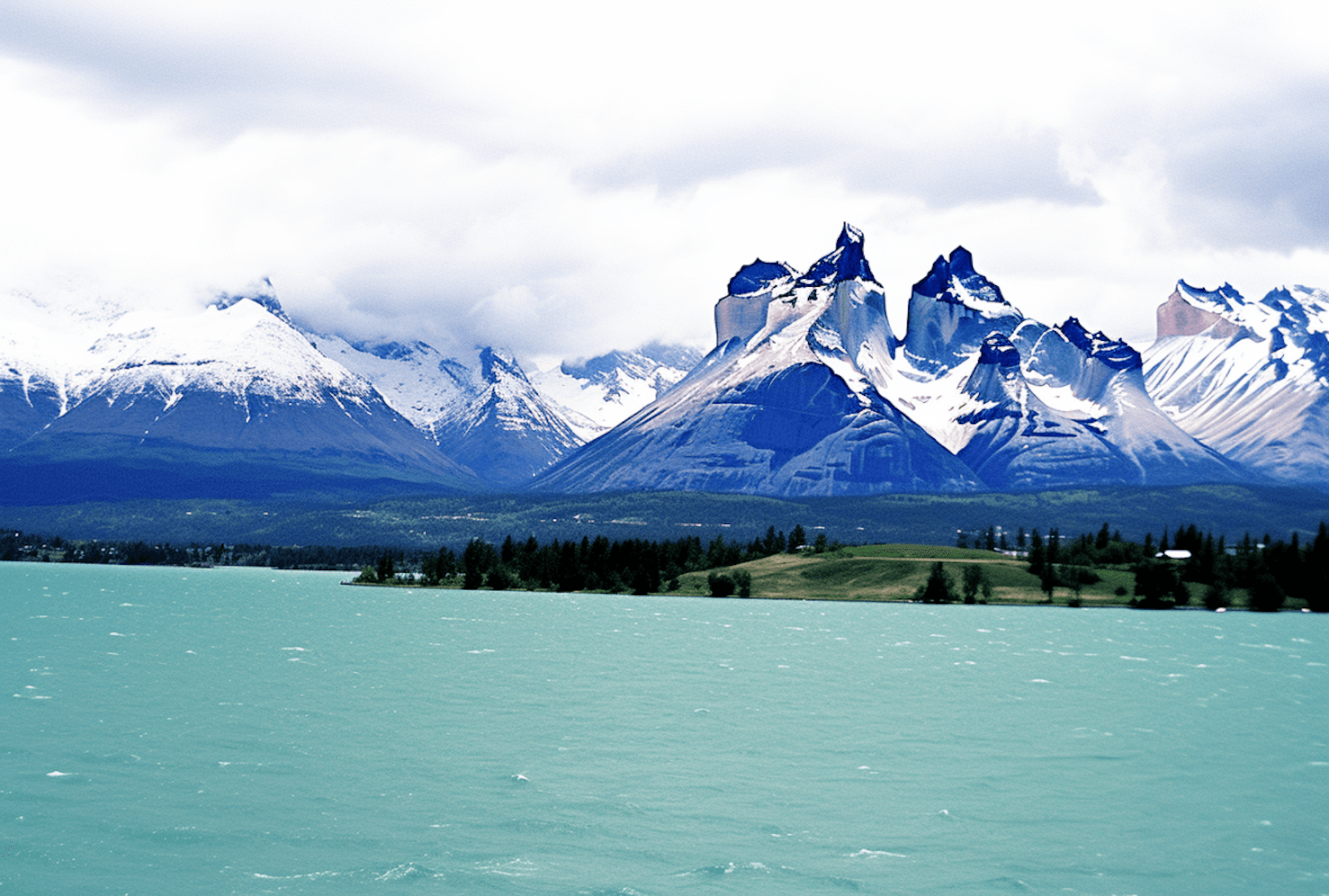 Jagged granite peaks dusted with snow rising behind a windswept turquoise lake