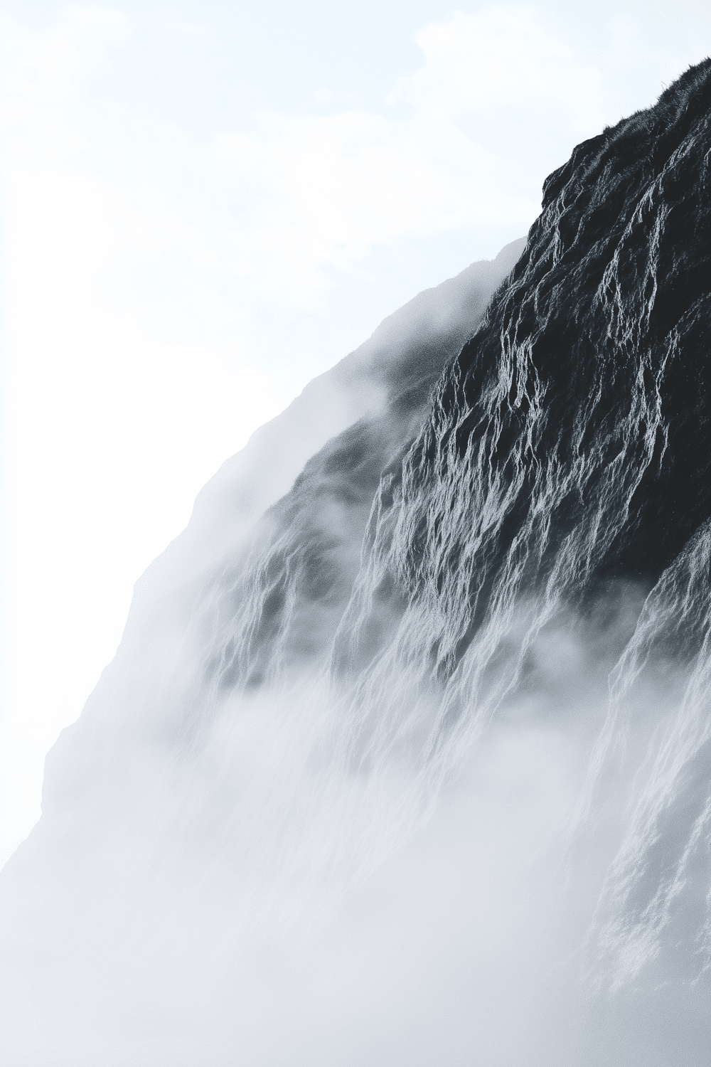 A dark, grass-topped cliff face disappearing into thick mist